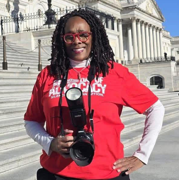 Chanta Jackson posing in a red shirt with a DSLR camera in her hand. The Capitol building in Washington DC is in the background.