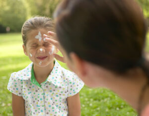 Image of young girl having sunscreen applied to face by an adult
