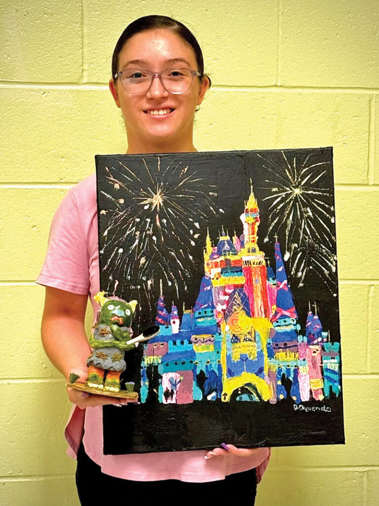 female student posing with painting of a castle and fireworks