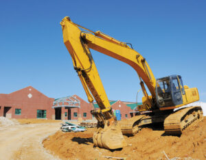Crane digging in dirt in front of a school building
