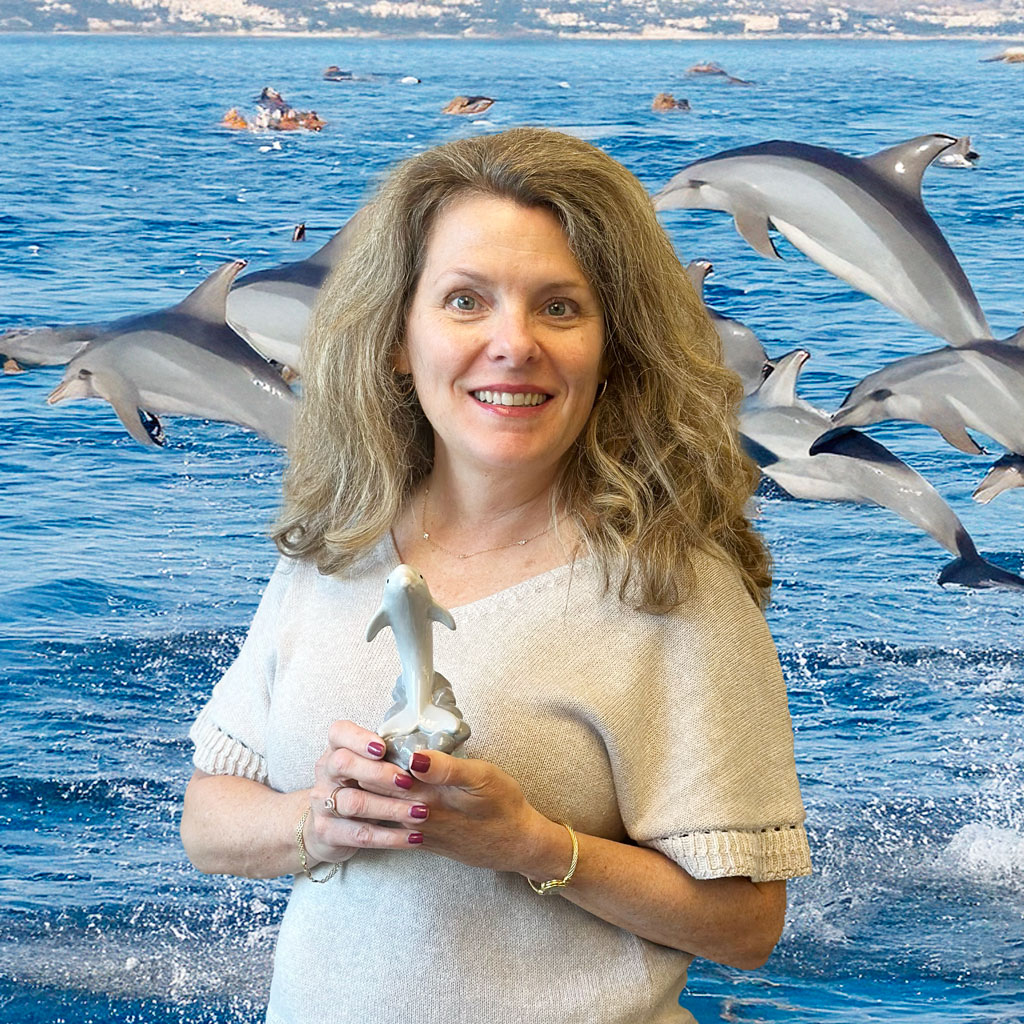 Laura Geltch posing with a dolphin figurine with a background of dolphins jumping in the ocean