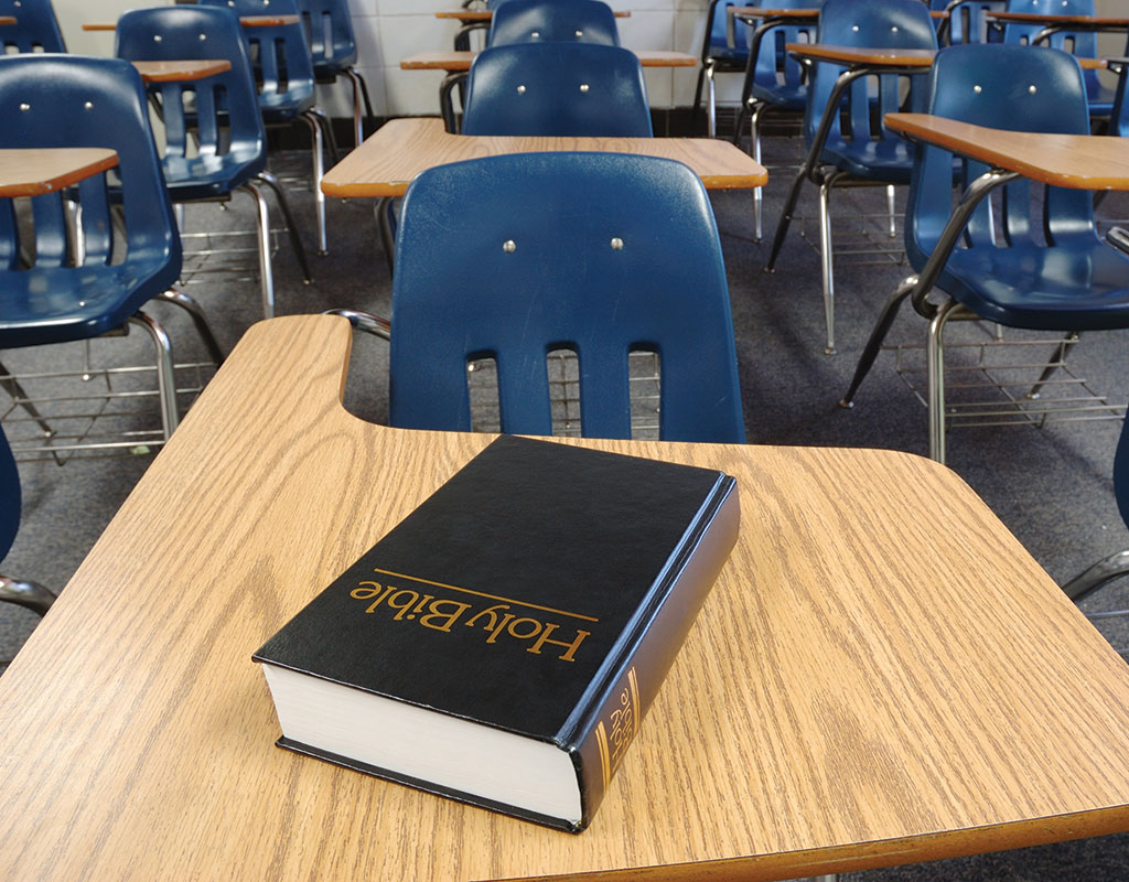 Photo of an empty desk in a classroom with a bible sitting on it