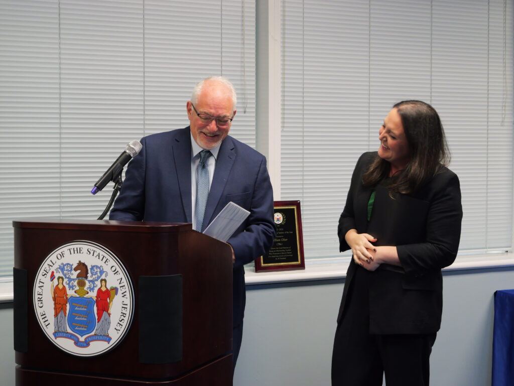 Jorden Schiff, Assistant Commissioner of the Division of Teaching and Learning Services laughing at podium with Gillian Ober, 2025-2026 Teacher of the Year.