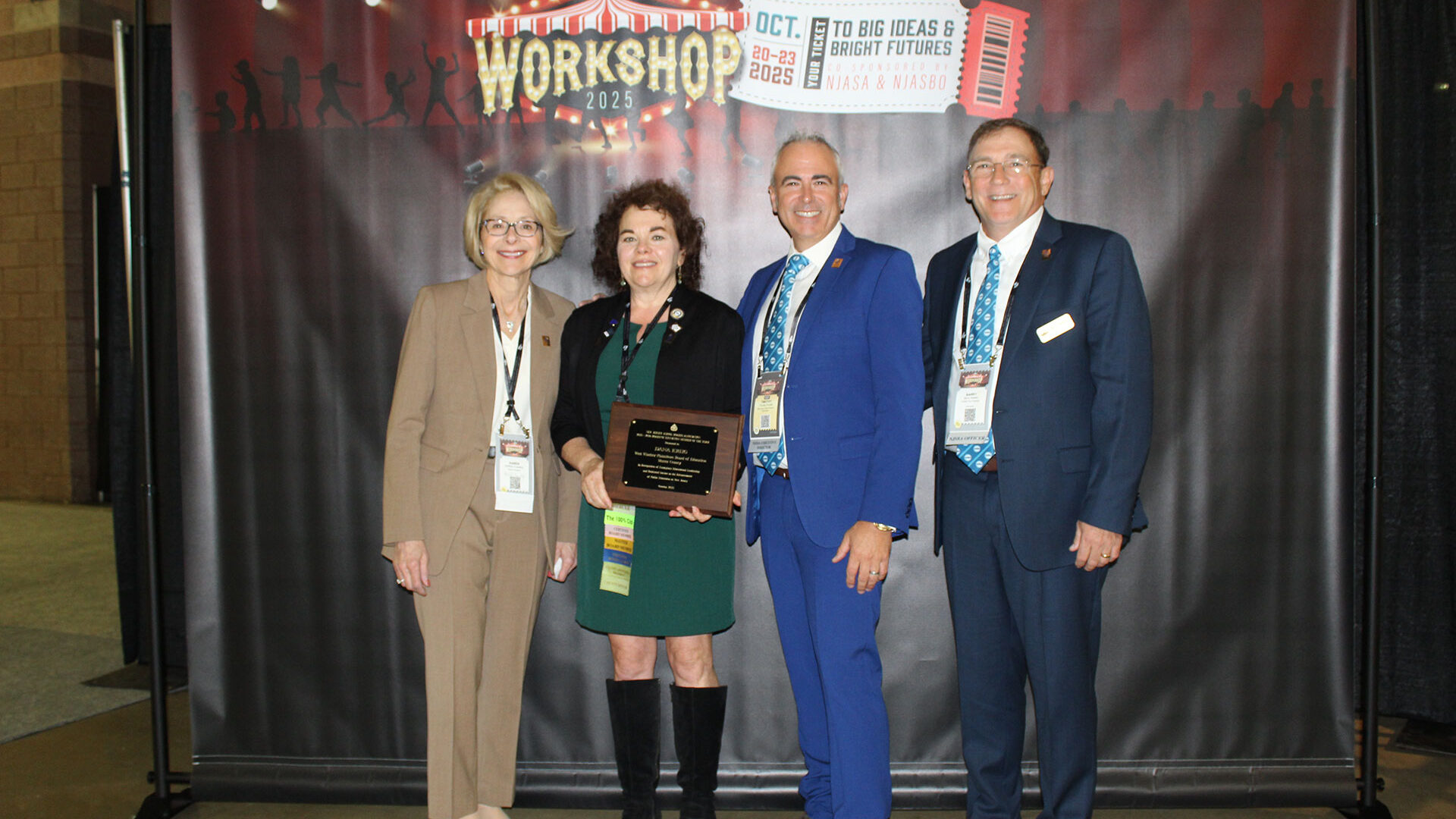 group of people posing holding a plaque with the workshop 2025 themed backdrop