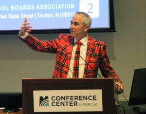 Dr. Timothy Purnell addresses the crowd at a podium wearing a red plaid suit