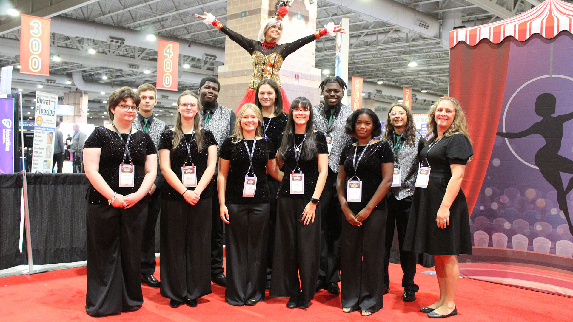 student choir posing with woman on stilts in front of the workshop 2025 entrance unit