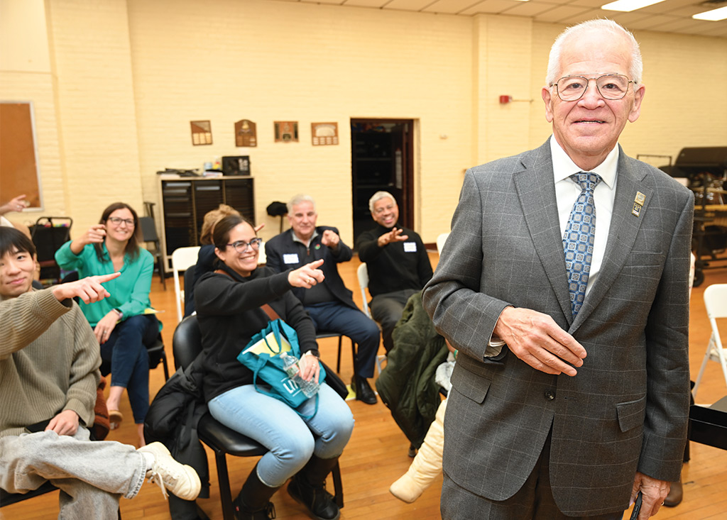Michael Jacobs poses in front of a crowd sitting in school desks, pointing and smiling at him