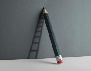 A lifesize gray pencil leans against a lighter gray wall casting a shadow of a ladder.