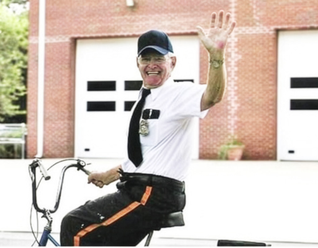 older male school security officer sitting on a bike smiling and waving