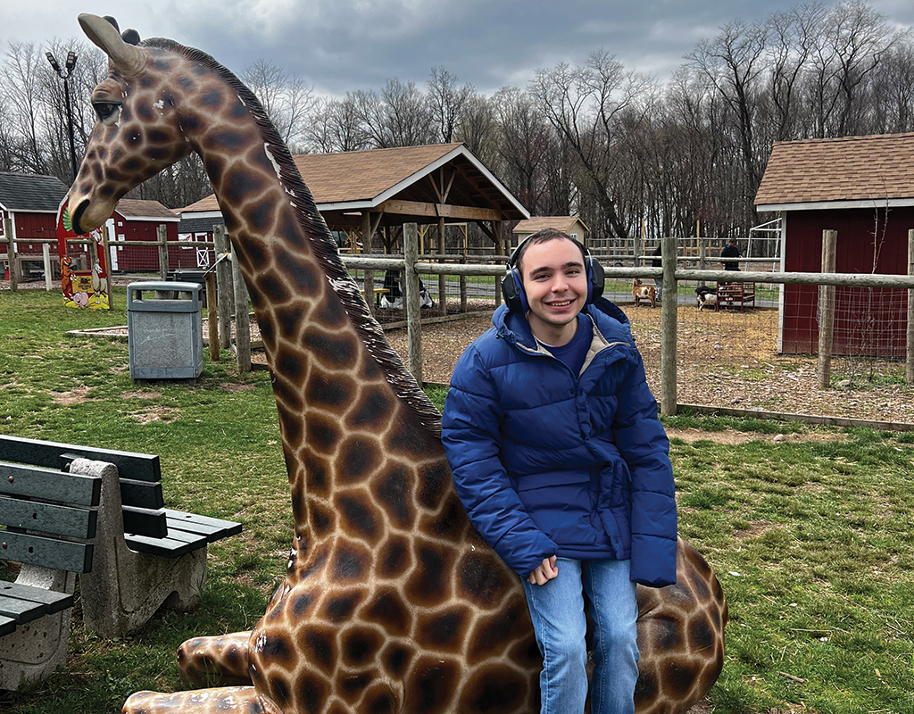 Special needs boy smiling and posing with a giraffe statue at a zoo