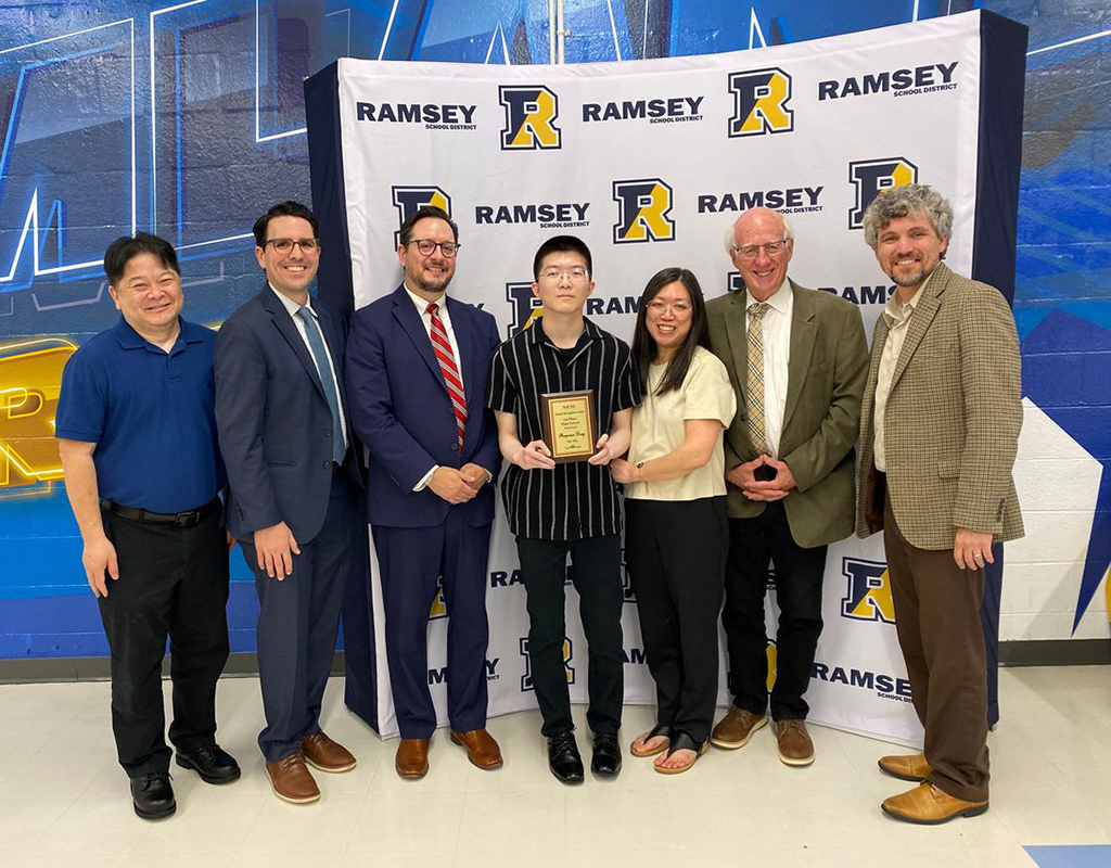 group of seven people in business attire pose with a plaque